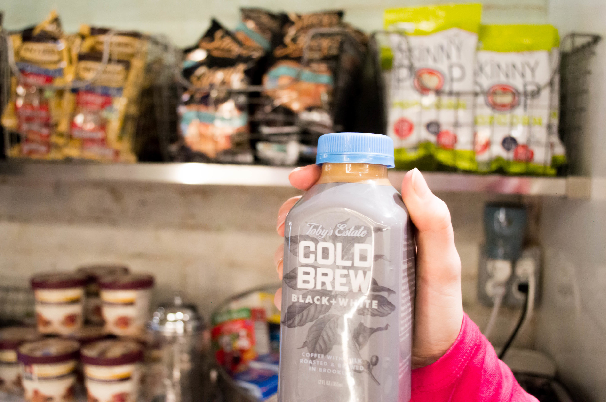 Bottle of cold brew coffee being held up in front of shelves of snacks