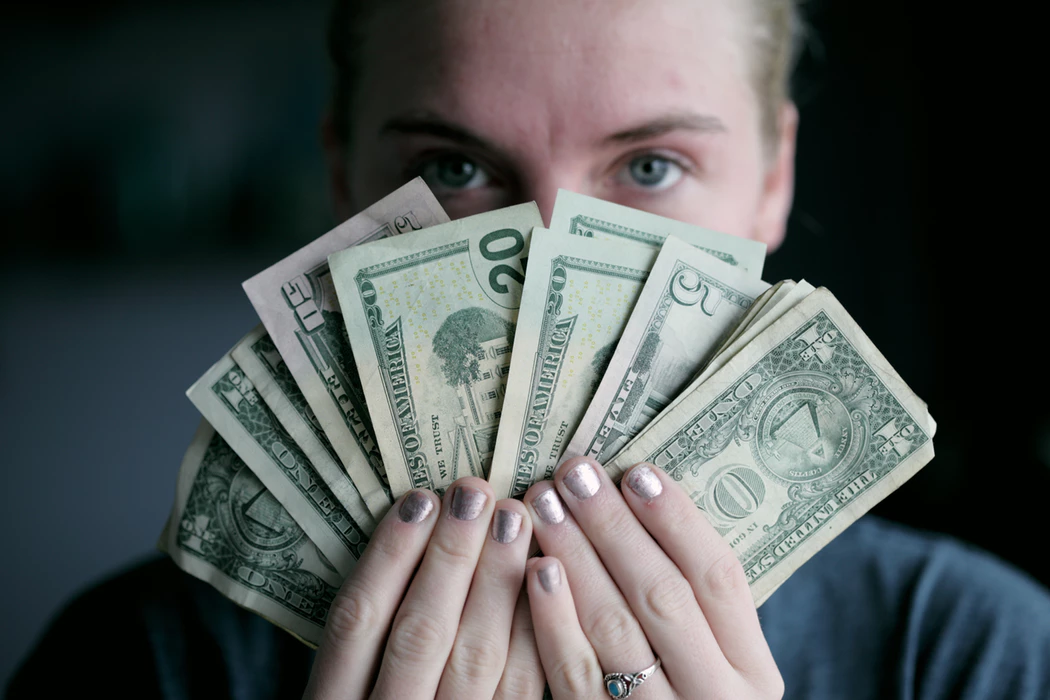 woman holding fanned out cash in front of her face