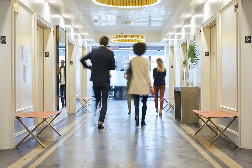 businesspeople walking down white hallway with several elevators