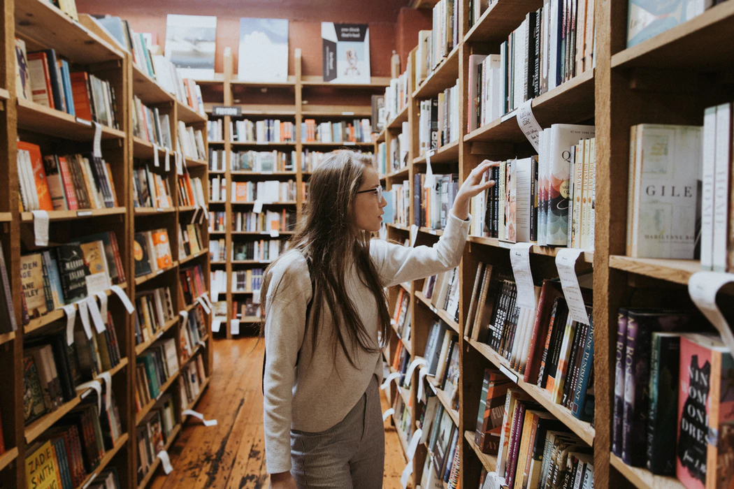 woman sifting through shelves of books at a bookstore or library