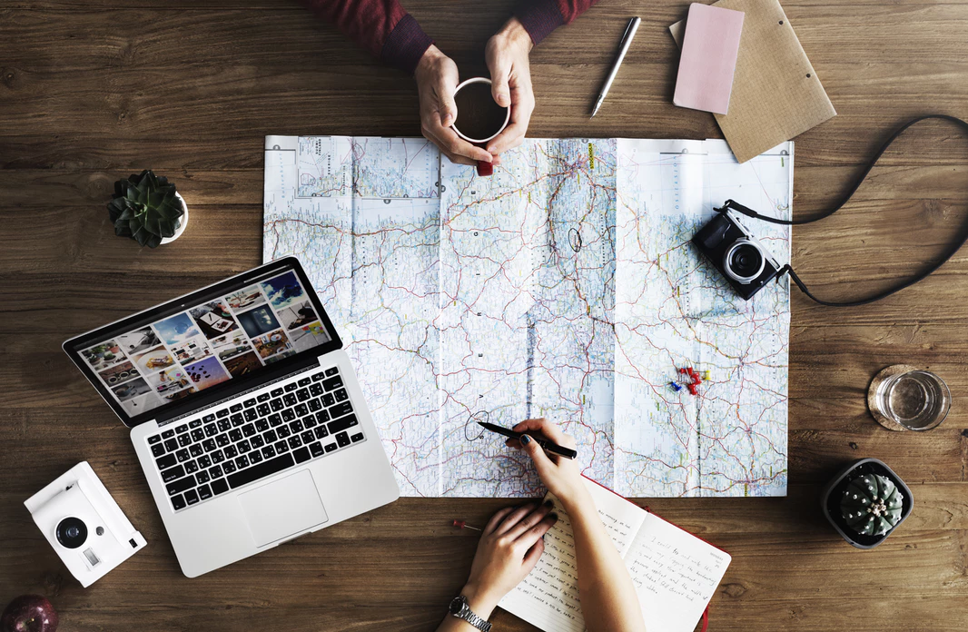 flat lay of map and laptop with other office items on wooden desk