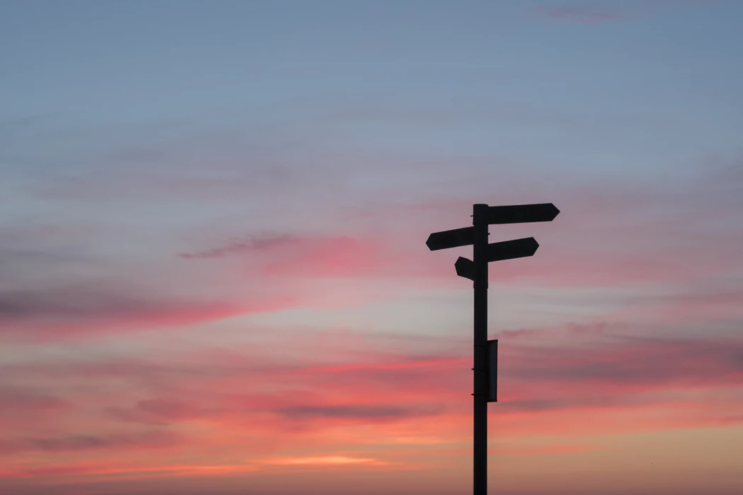 multi-directional signs on a post with sunset sky in the background