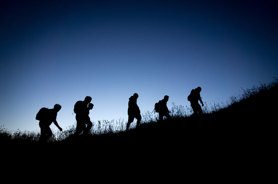 silhouettes of hikers climbing a grassy hill