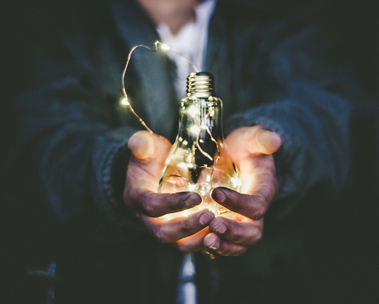 man in jacket holding a lightbulb with string lights inside