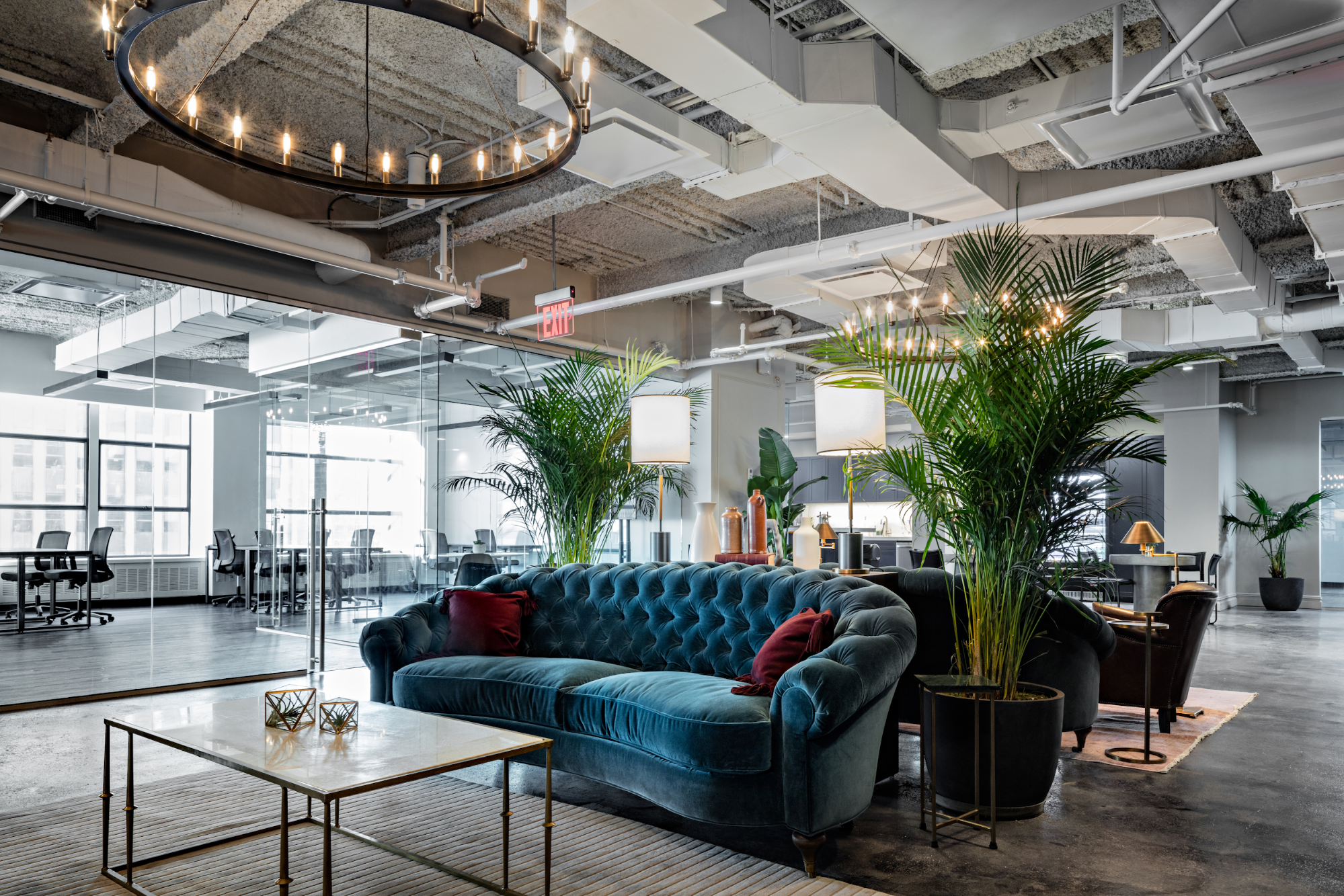 bright open-concept coworking office in a renovated industrial space, with large chandeliers and colorful couches