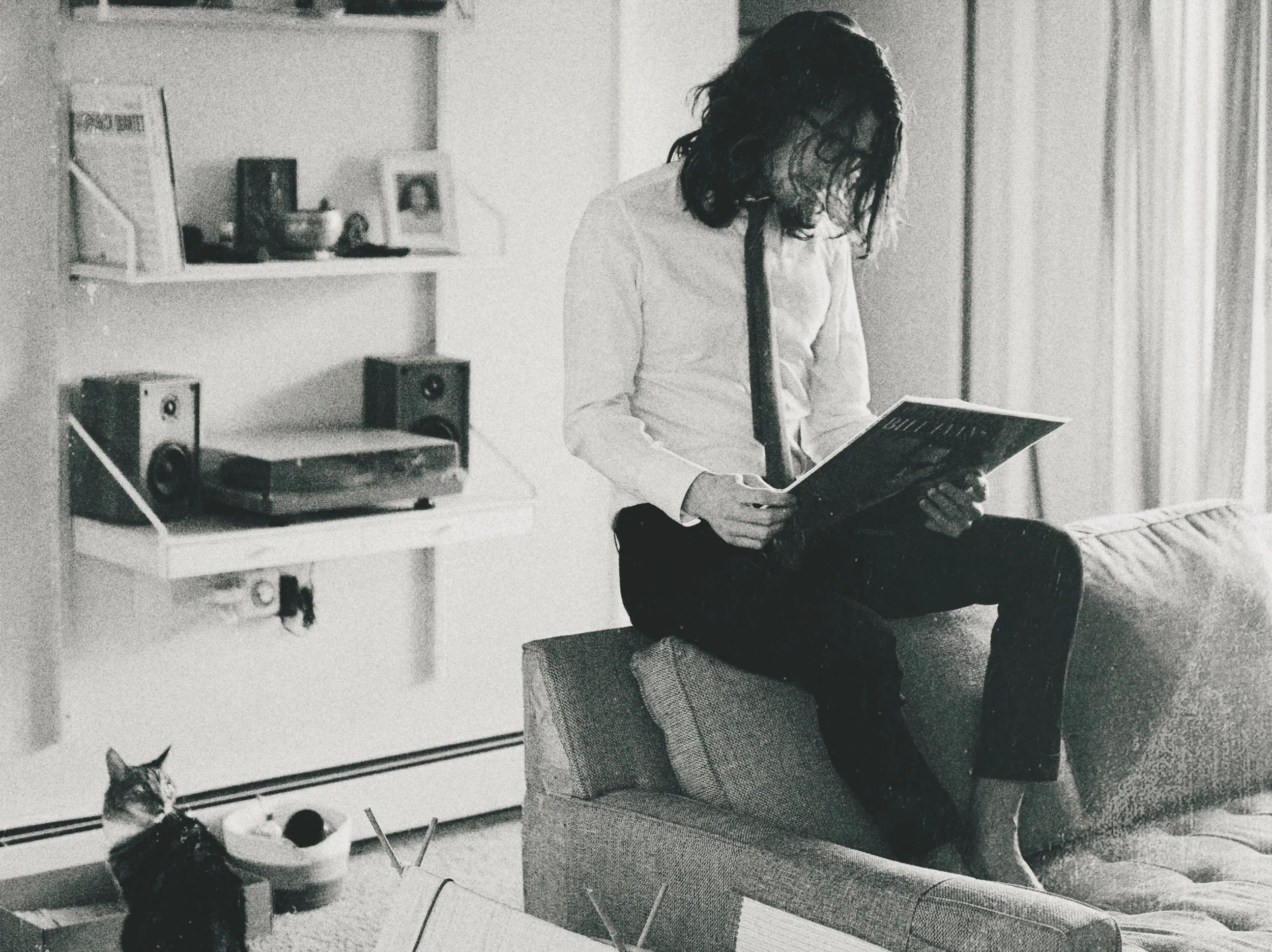 A Black & White photo of Chris Swartwood sitting on a couch looking at the back of a vinyl album.