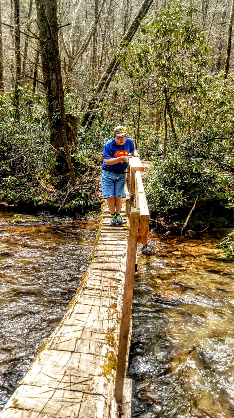   James crosses a bridge over a stream on one of his outdoor adventures.  