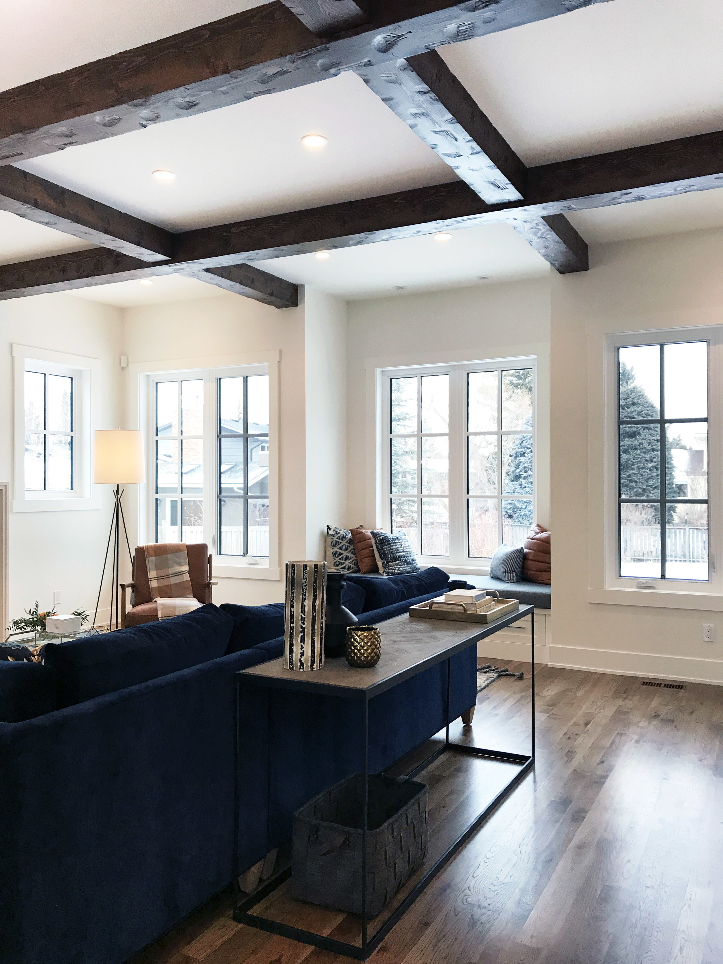 Family focused living space with wood beam ceiling detail and navy chenille sectional. Interior Design by Nyla Free Designs, Build by Veranda Estate Homes