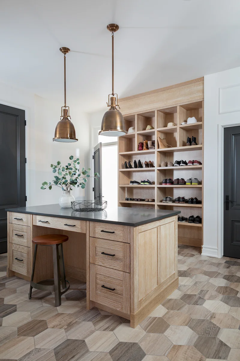 The mudroom with “wood-like” large hex floor tiles, custom built-in cabinetry and island for extra storage from a Rural Alberta Country House, Interior Design by Calgary Design Studio Nyla Free Designs Inc, Photography: Phil Crozier #calgaryinteriordesign #calgaryinteriordesigner #nylafreedesigns #mudroominspirations #countryhouse