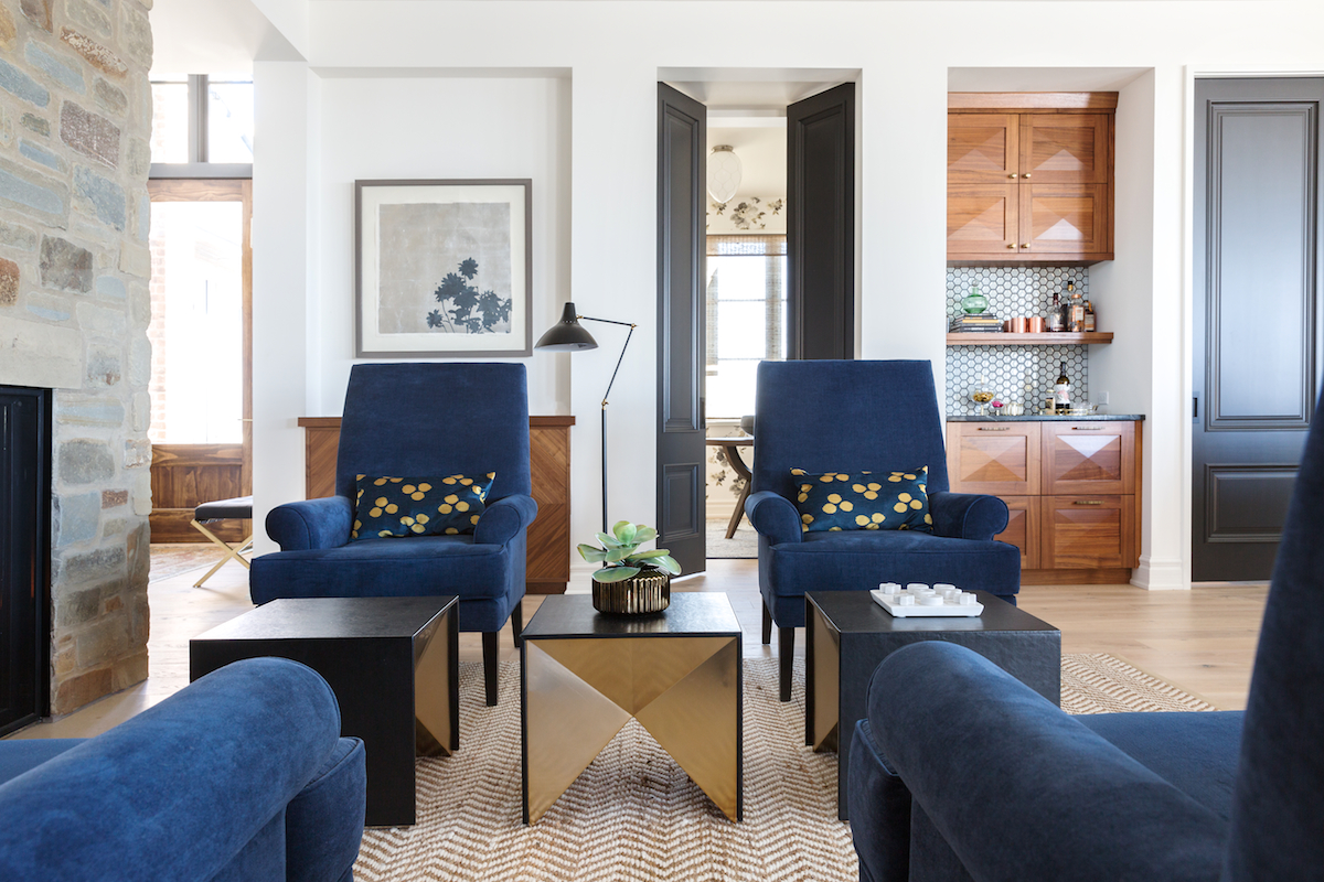 A sitting room with 4 navy chairs in front of a stone fireplace from a Rural Alberta Country House, Interior Design by Calgary Design Studio Nyla Free Designs Inc, Architecture: Dejong Design Associates, Photography: Phil Crozier #calgaryinteriordesign #calgaryinteriordesigner #nylafreedesigns #sittingroominspirations #countryhouse