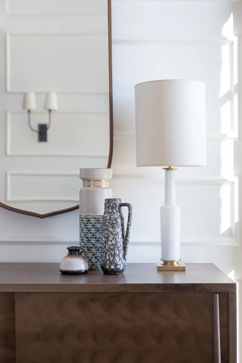 A welcoming front entry with table lamps, wall sconces and vintage vases from a Rural Alberta Country House, Interior Design by Calgary Design Studio Nyla Free Designs Inc, Photography: Phil Crozier, #nylafreedesigns #calgaryinteriordesigners #blackdoors #wallpanelling #countryhouse #styledpretty