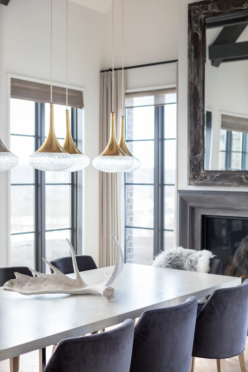 The dining room with seating for ten, fireplace and hanging pendants from a Rural Alberta Country House, Interior Design by Calgary Design Studio Nyla Free Designs Inc, Architecture: Dejong Design Associates, Photography: Phil Crozier #calgaryinteriordesign #calgaryinteriordesigner #nylafreedesigns #diningroominspirations #countryhouse