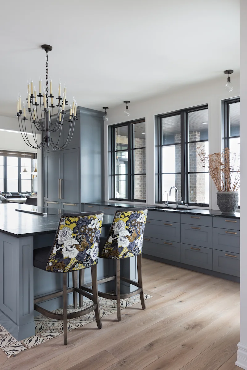 The kitchen with off-set chandelier, counter stool at end of island, panelled fridges and windows extending over the counter from a Rural Alberta Country House, Interior Design by Calgary Design Studio Nyla Free Designs Inc, Architecture: Dejong Design Associates, Photography: Phil Crozier #calgaryinteriordesign #calgaryinteriordesigner #nylafreedesigns #kitcheninspirations #countryhouse