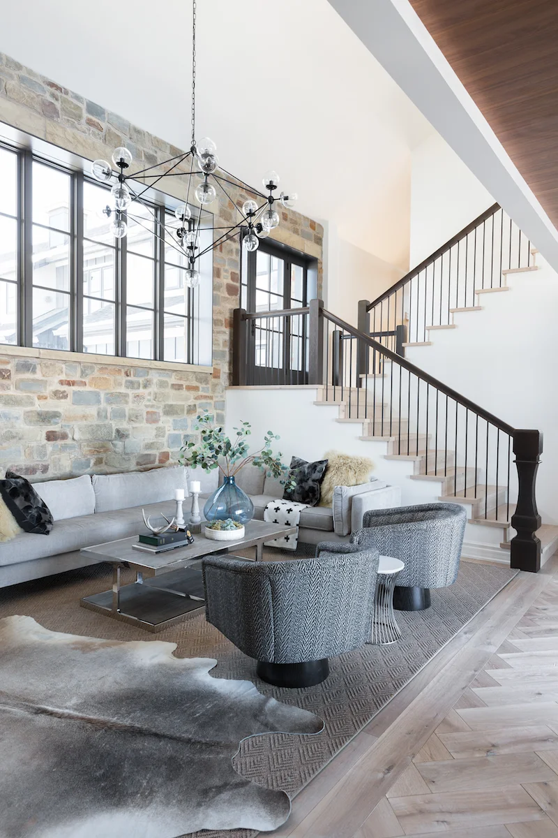A Living Room with feature stone wall, layered carpets and custom furniture from a Rural Alberta Country House, Interior Design by Calgary Design Studio Nyla Free Designs Inc, Architecture: Dejong Design Associates, Photography: Phil Crozier #calgaryinteriordesign #calgaryinteriordesigner #nylafreedesigns #livingessentials #countryhouse
