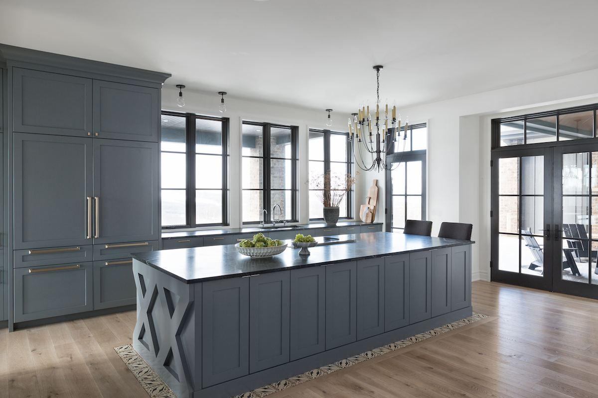 The kitchen with a cooktop in the island, panelled fridges and windows extending over the counters from a Rural Alberta Country House, Interior Design by Calgary Design Studio Nyla Free Designs Inc, Architecture: Dejong Design Associates, Photography: Phil Crozier #calgaryinteriordesign #calgaryinteriordesigner #nylafreedesigns #kitcheninspirations #countryhouse