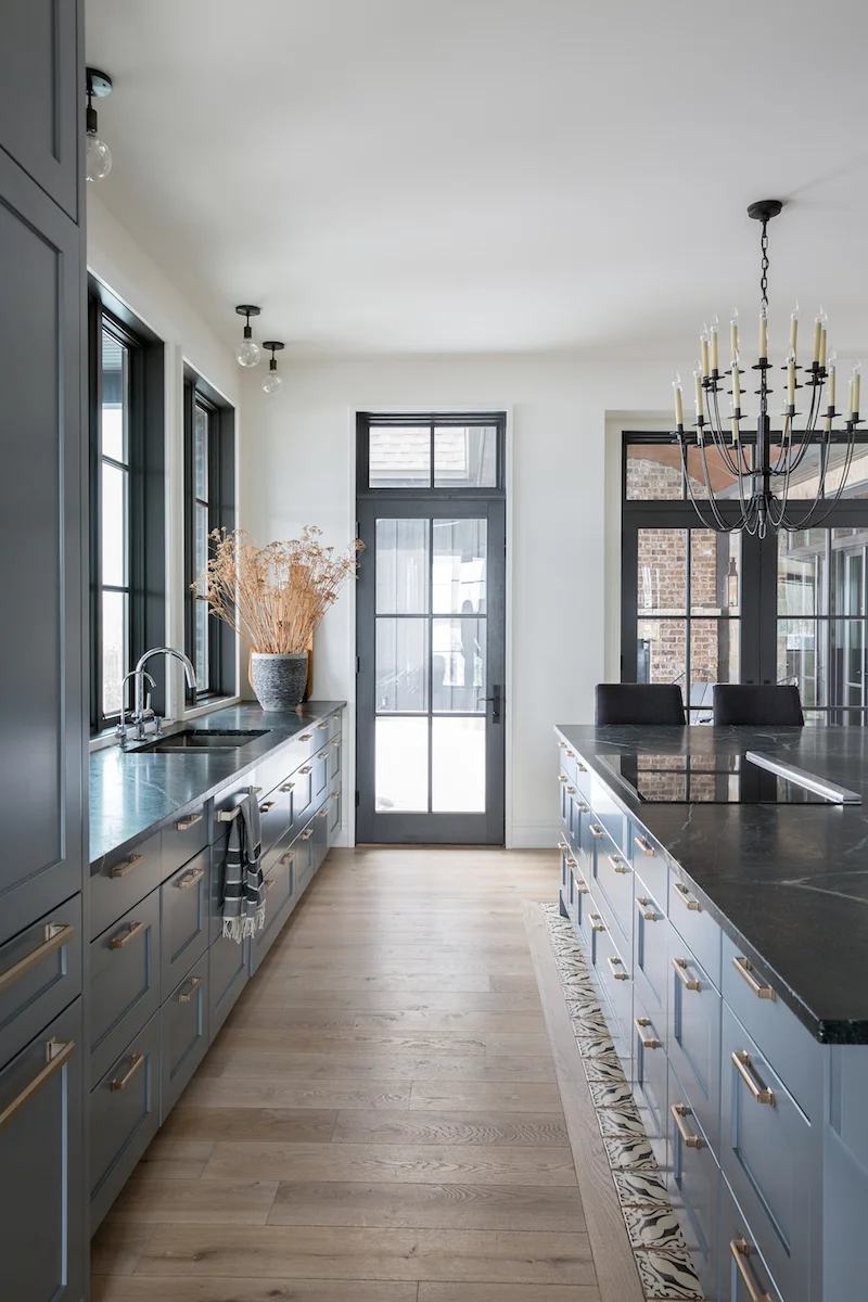 The kitchen with a cooktop in the island, panelled fridges and windows extending over the counters from a Rural Alberta Country House, Interior Design by Calgary Design Studio Nyla Free Designs Inc, Architecture: Dejong Design Associates, Photography: Phil Crozier #calgaryinteriordesign #calgaryinteriordesigner #nylafreedesigns #kitcheninspirations #countryhouse