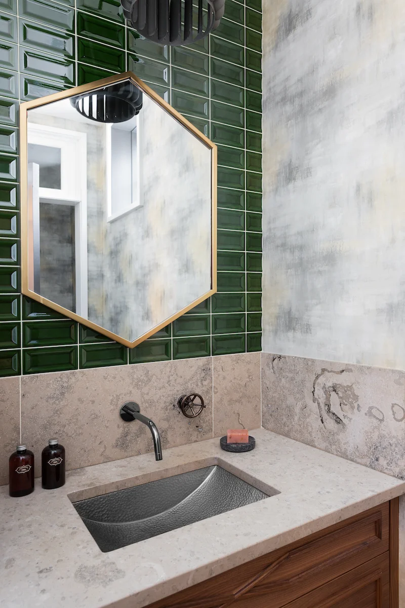 The powder room with Kelly green subway tile backsplash, limestone counters, and hammered sink from a Rural Alberta Country House, Interior Design by Calgary Design Studio Nyla Free Designs Inc, Photography: Phil Crozier #calgaryinteriordesign #calgaryinteriordesigner #nylafreedesigns #powderroominspirations #countryhouse