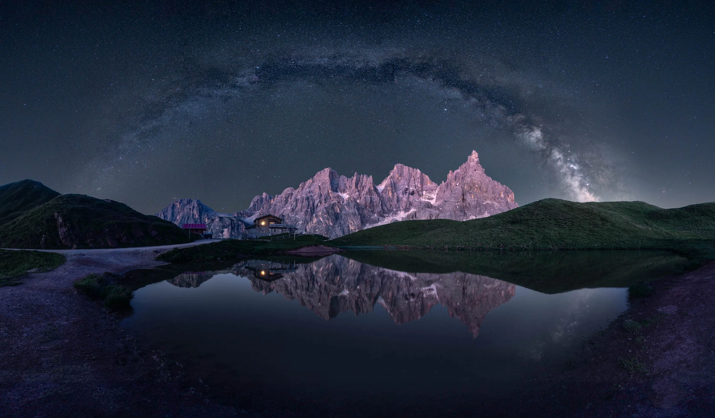 Panoramic nightscape of Baita Segantini and Pale die San Martino under the milky way arch. 