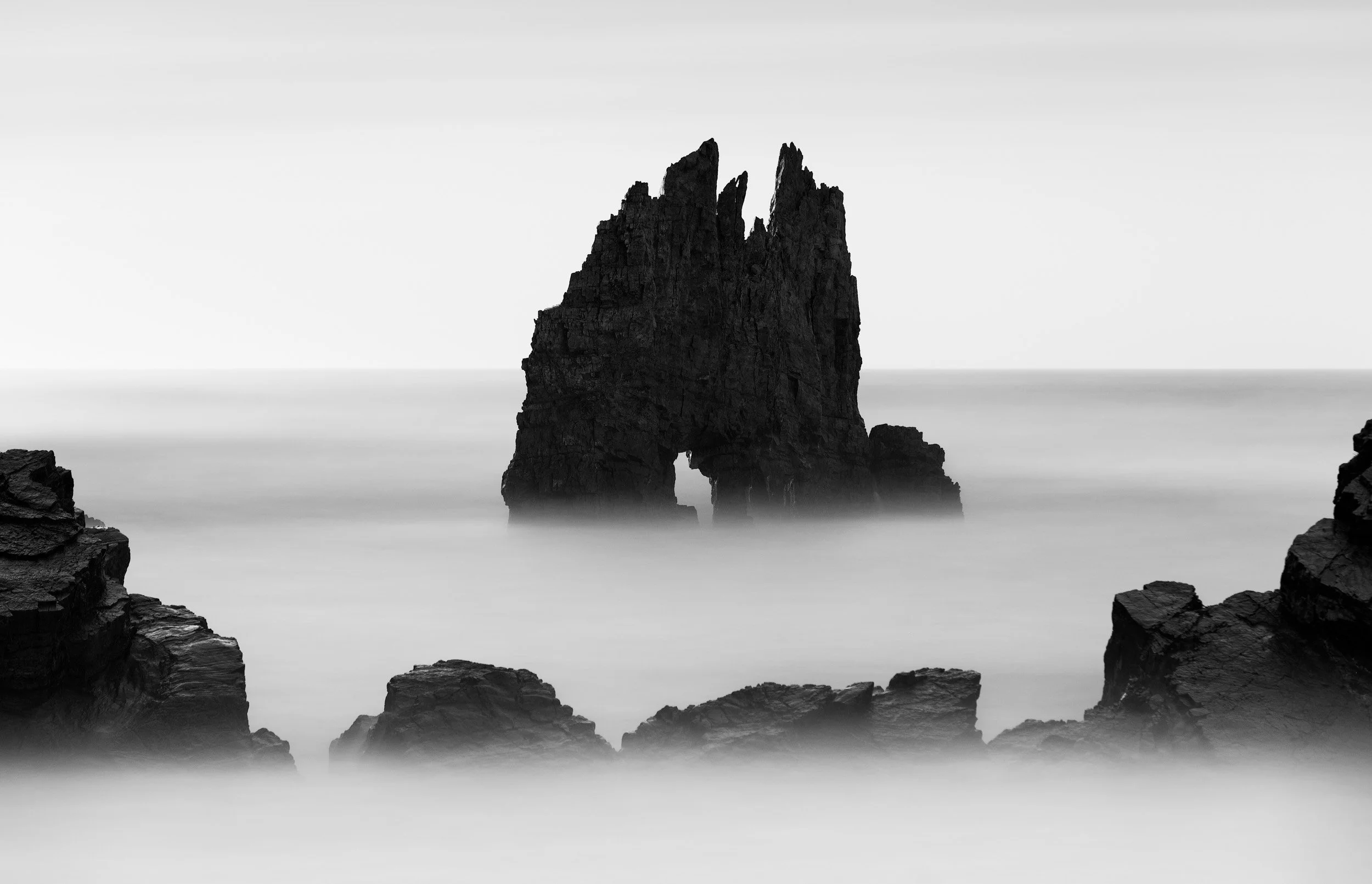 Black and white long exposure fine-art image of a sharp, spiky rock formation at the playa de portizuelo in the region of Asturias in northern Spain. 