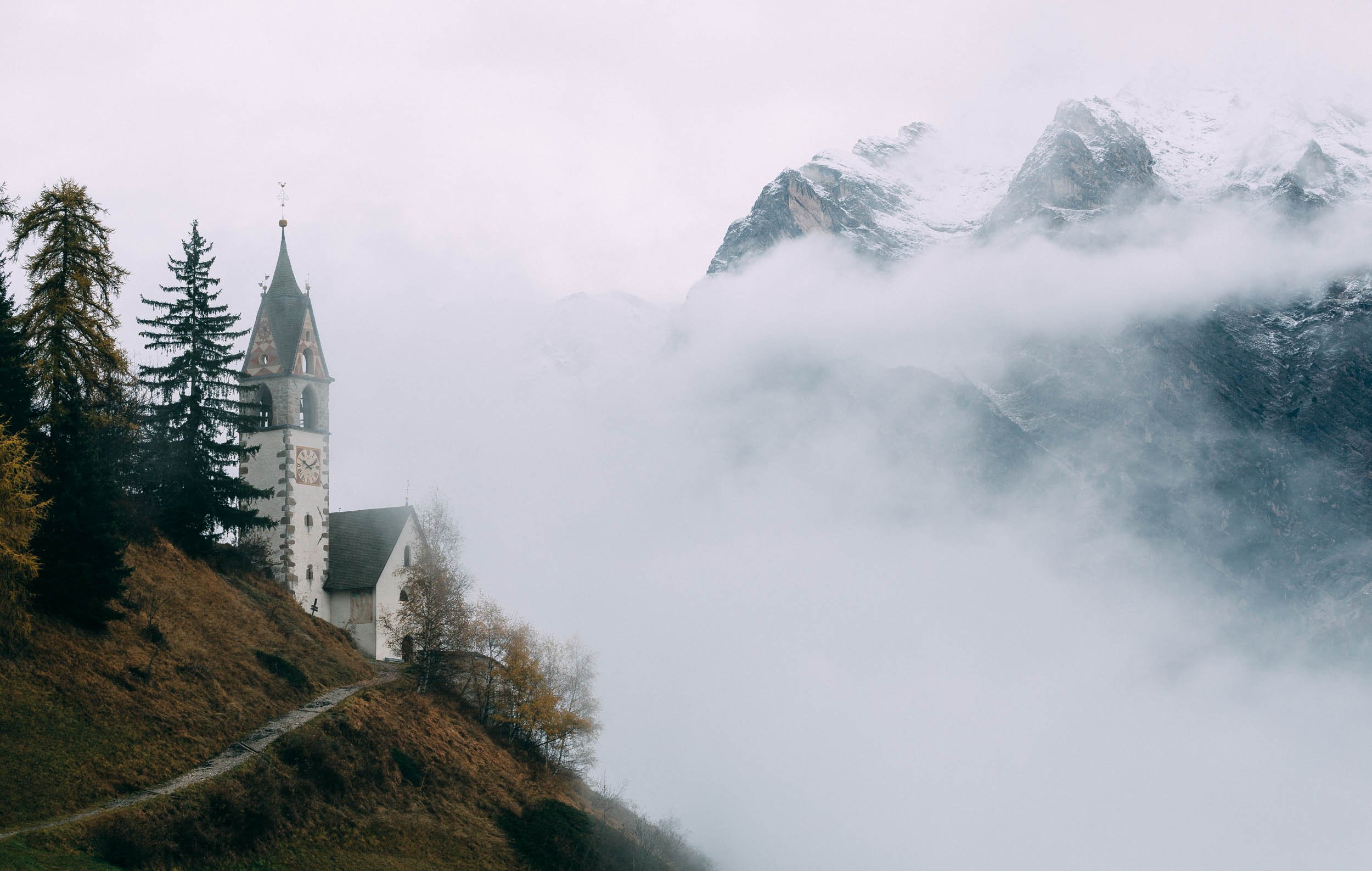 Kapelle zur Hl. Barbara in the Dolomites in front of mountain range covered in clouds. 