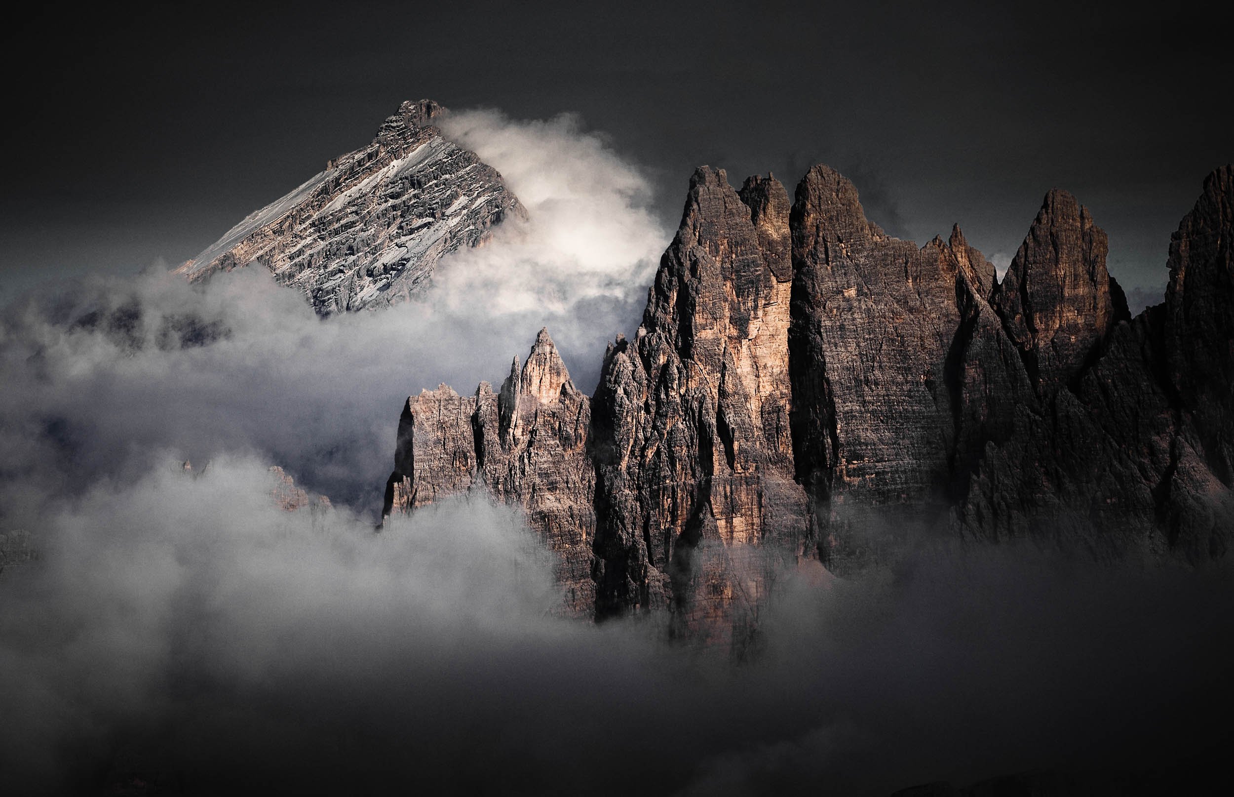 Ragged peaks of the Croda da Lago mountain group in the Italian Dolomites surrounded by clouds.