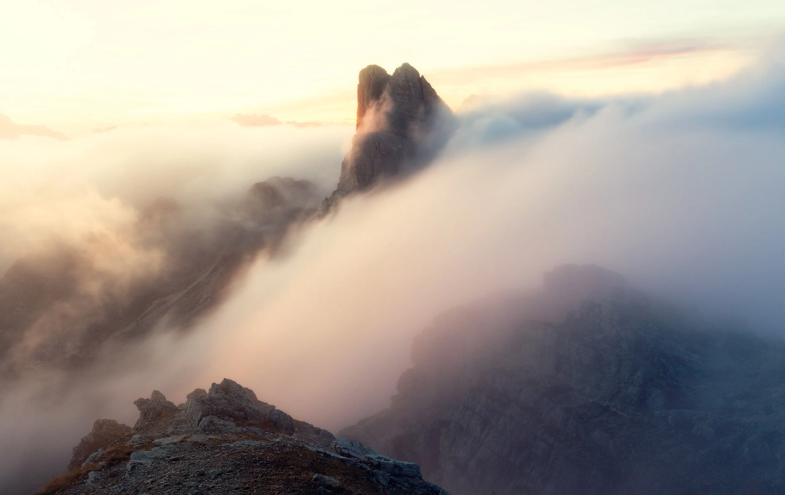 A sea of clouds surrounding the mountain peak of Monte Averau during sunset in the Italian Dolomites.