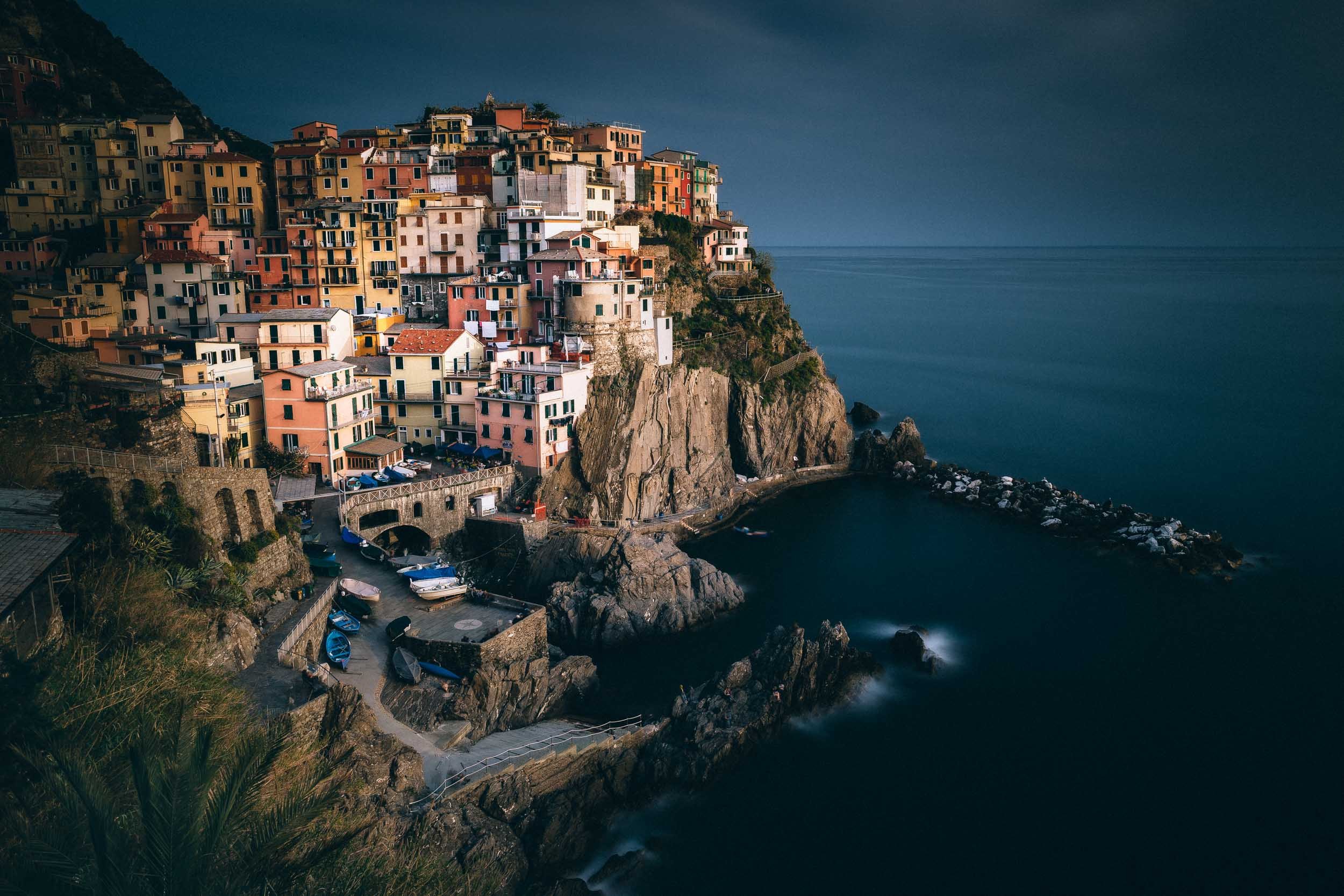 The colorful houses of Manarola, Cinque Terre in Italy during a moody blue hour seen from the hills above the city. 
