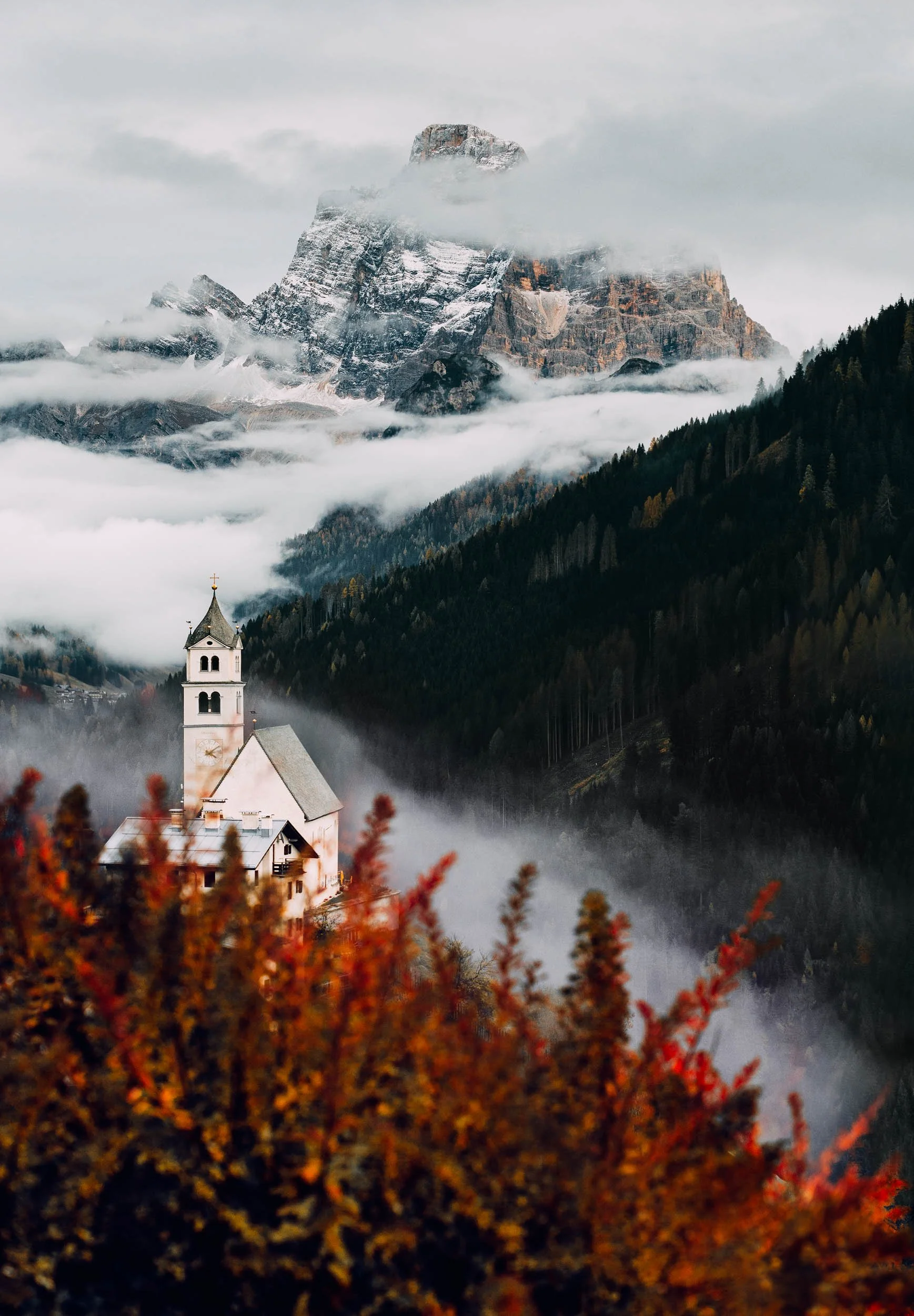 Chiesa di Colle Santa Lucia framed by a red bush and snowy Monte Pelmo.