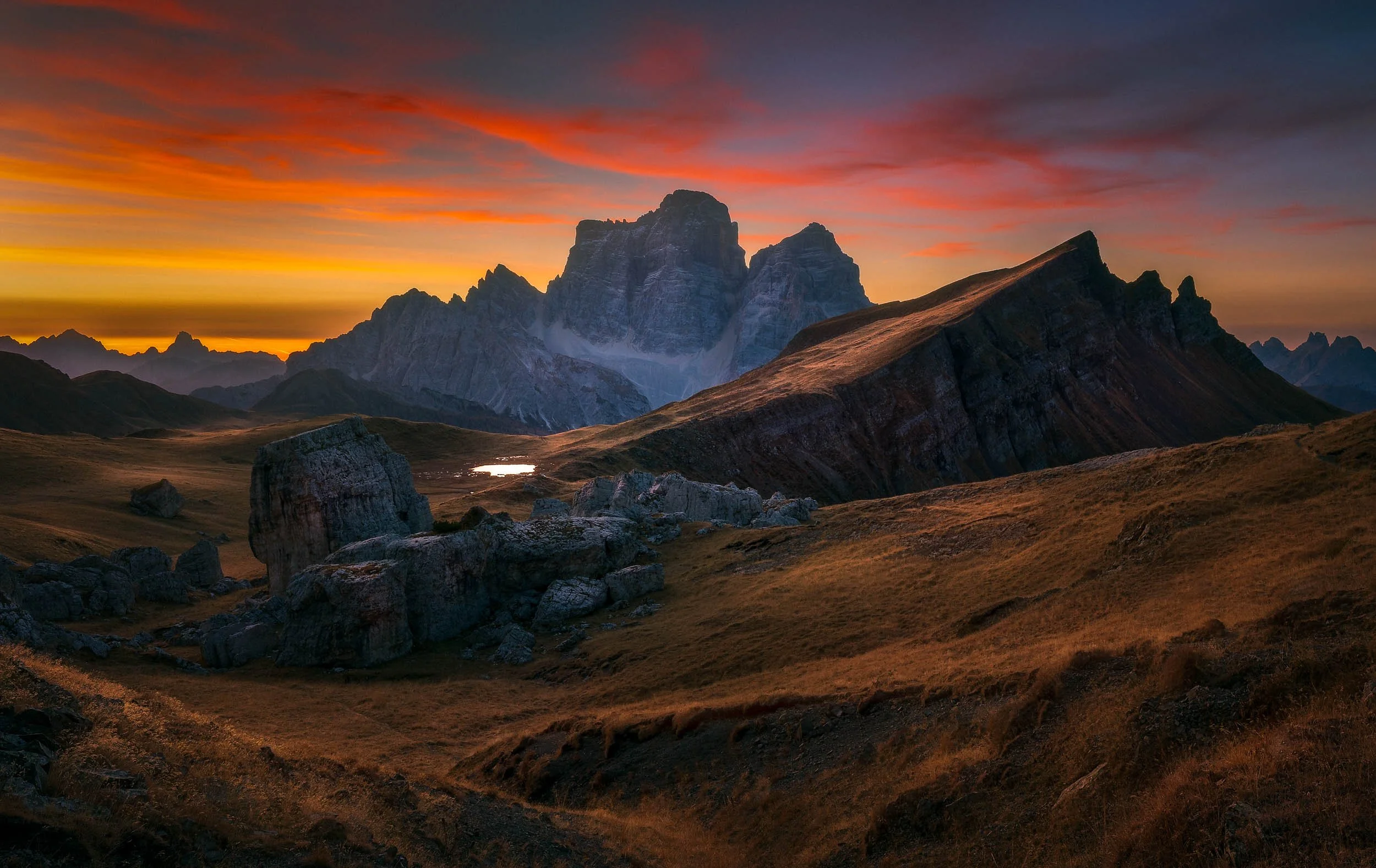 Malga Mondeval with its big boulders scattered in the valley during a colorufl autumn sunrise with Monte Pelmo towering in the background.