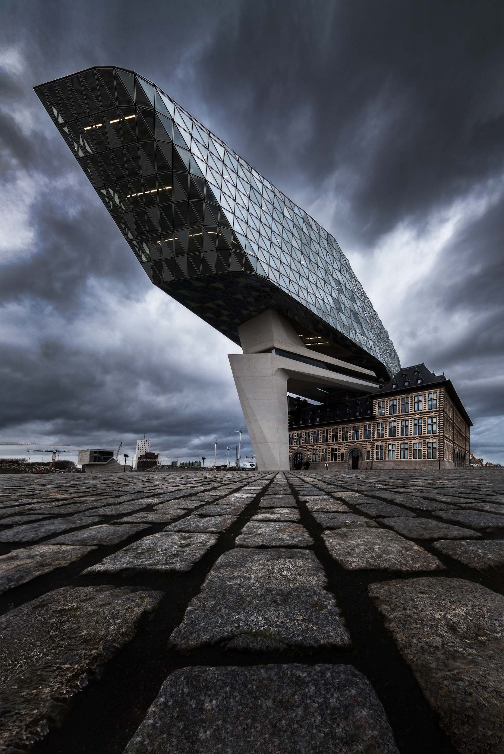 Wide angle photo of the port house in Antwerp, Belgium designed by Zaha Hadid under a dramatic, cloudy sky. 