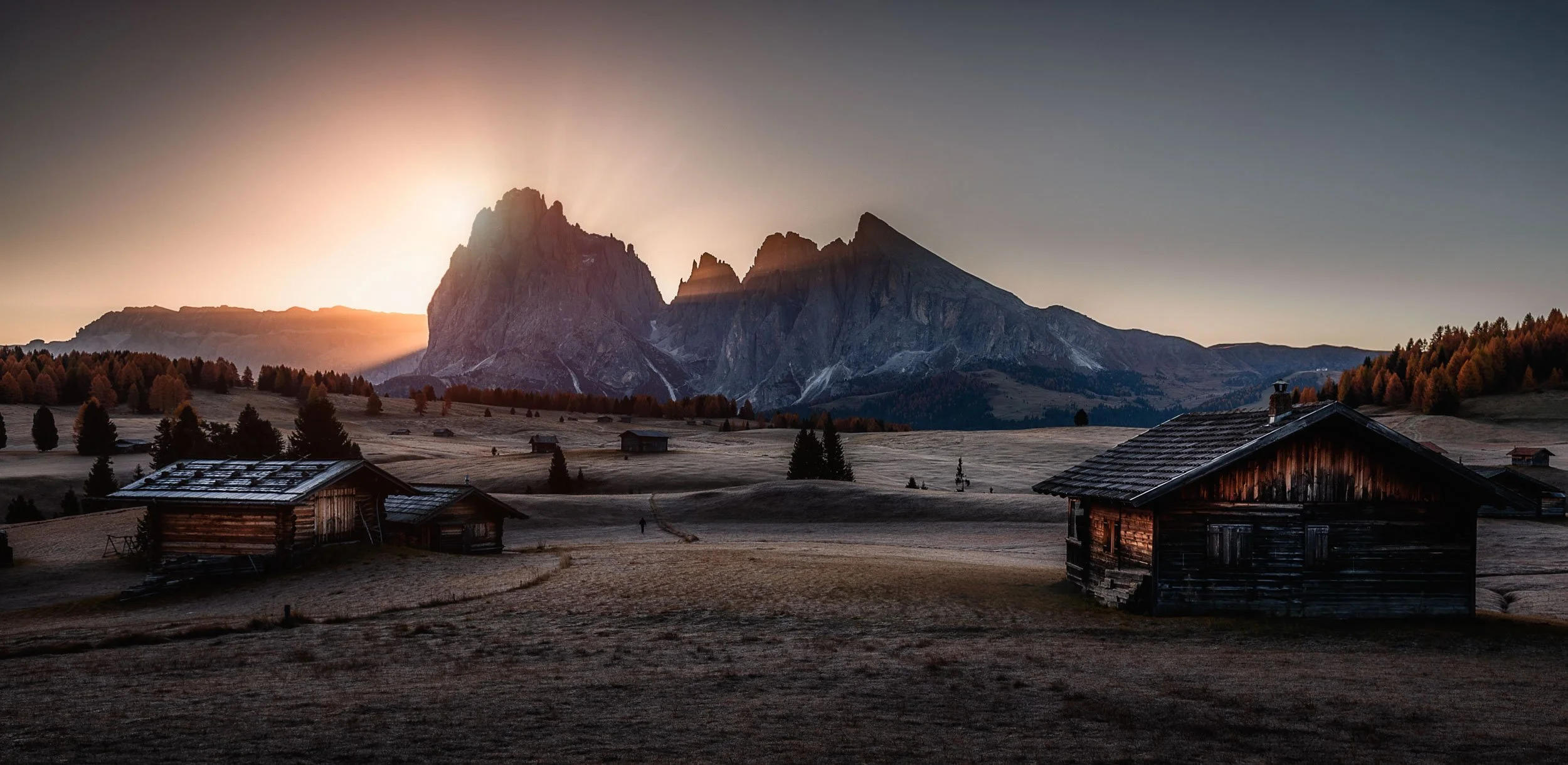 Alpe di Siusi during sunrsie with alpine cabins in front of the mountain peaks of Langkofel and Plattkofel. 
