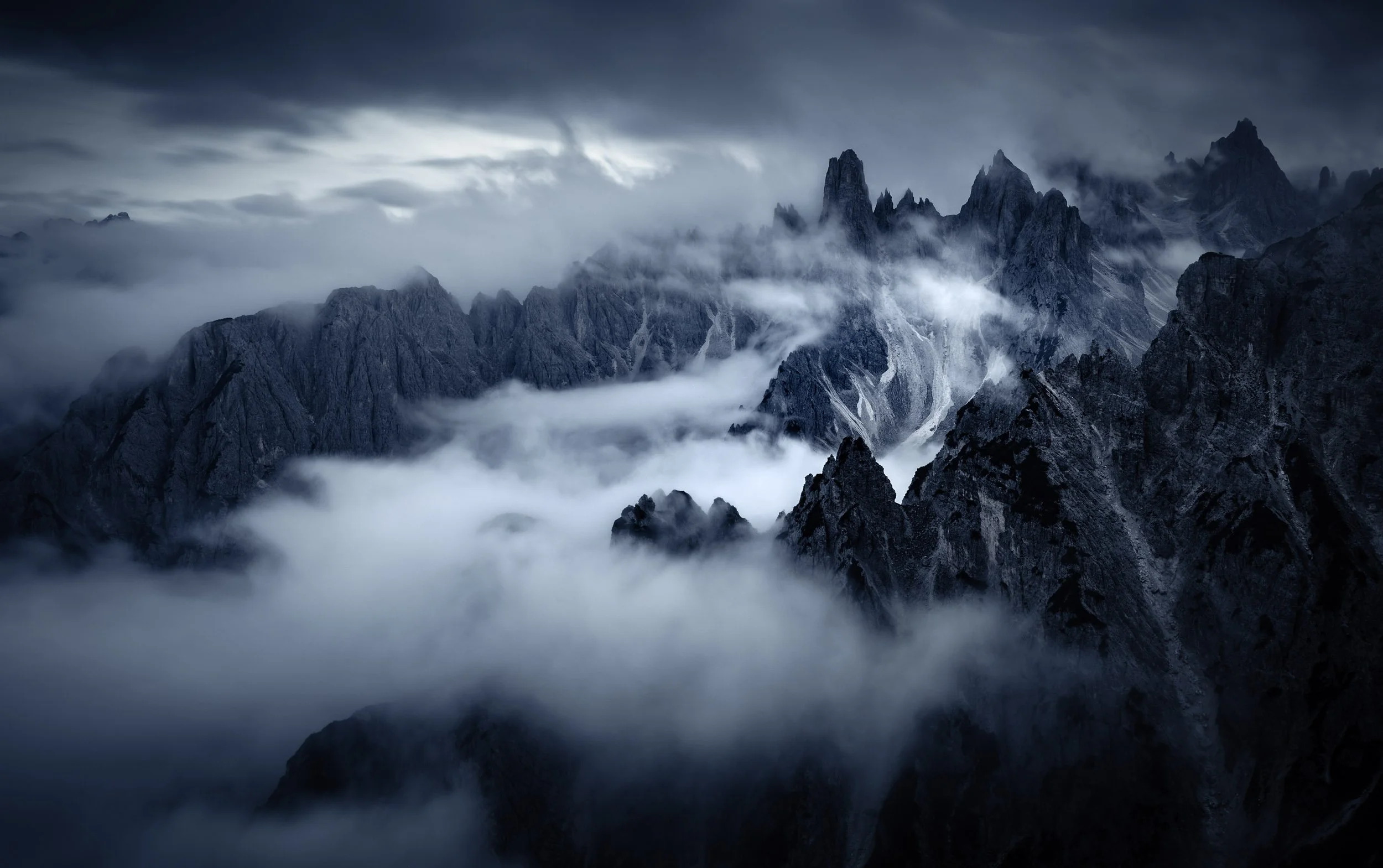 The ragged, sharp peaks of the Cima Cadini mountain group of the Italian Dolomites surrounded by clouds during the blue hour. 