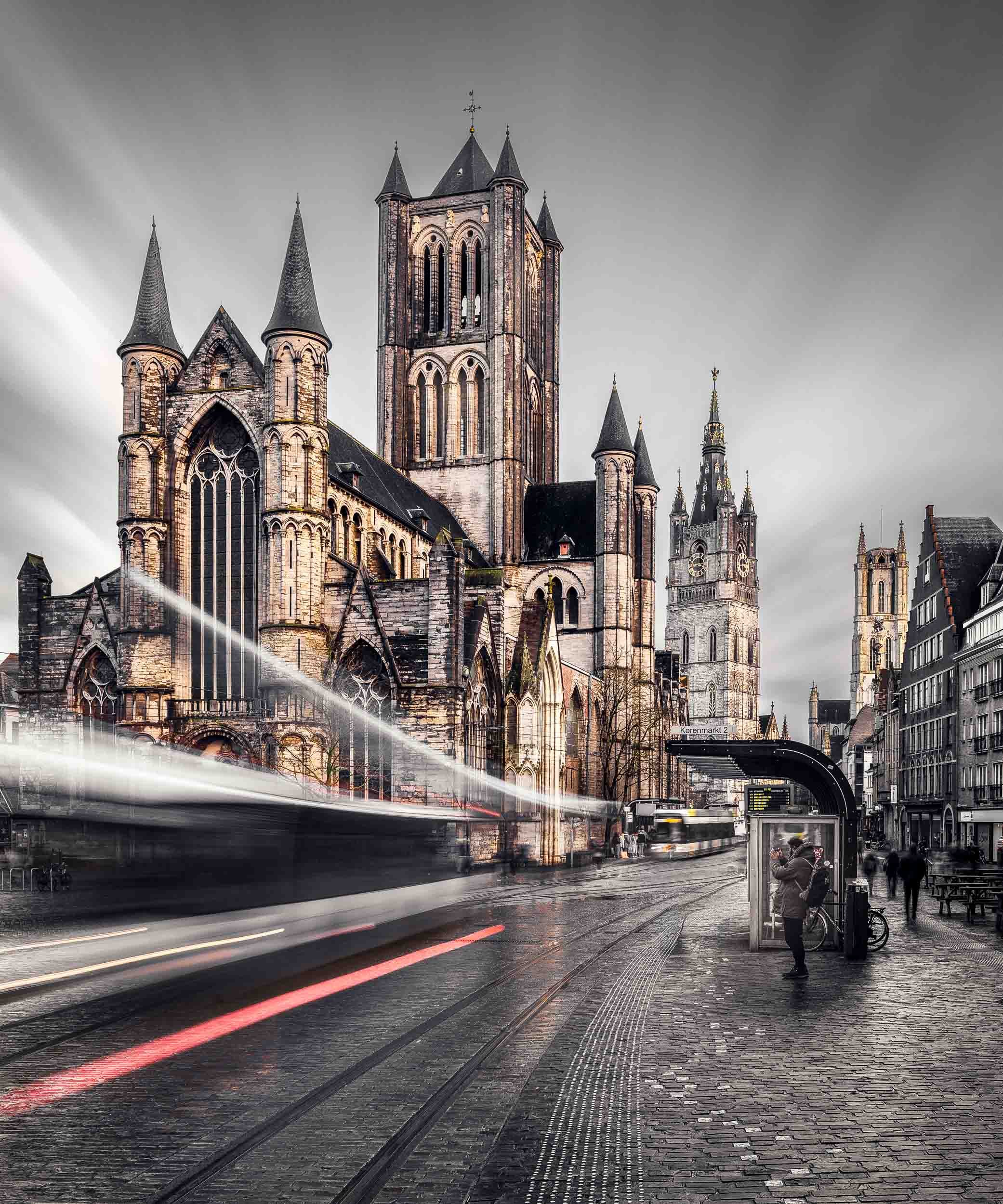 Long exposure photo of Saint Bavo cathedral in Ghent, Belgium with streaky clouds and a train rushing by.