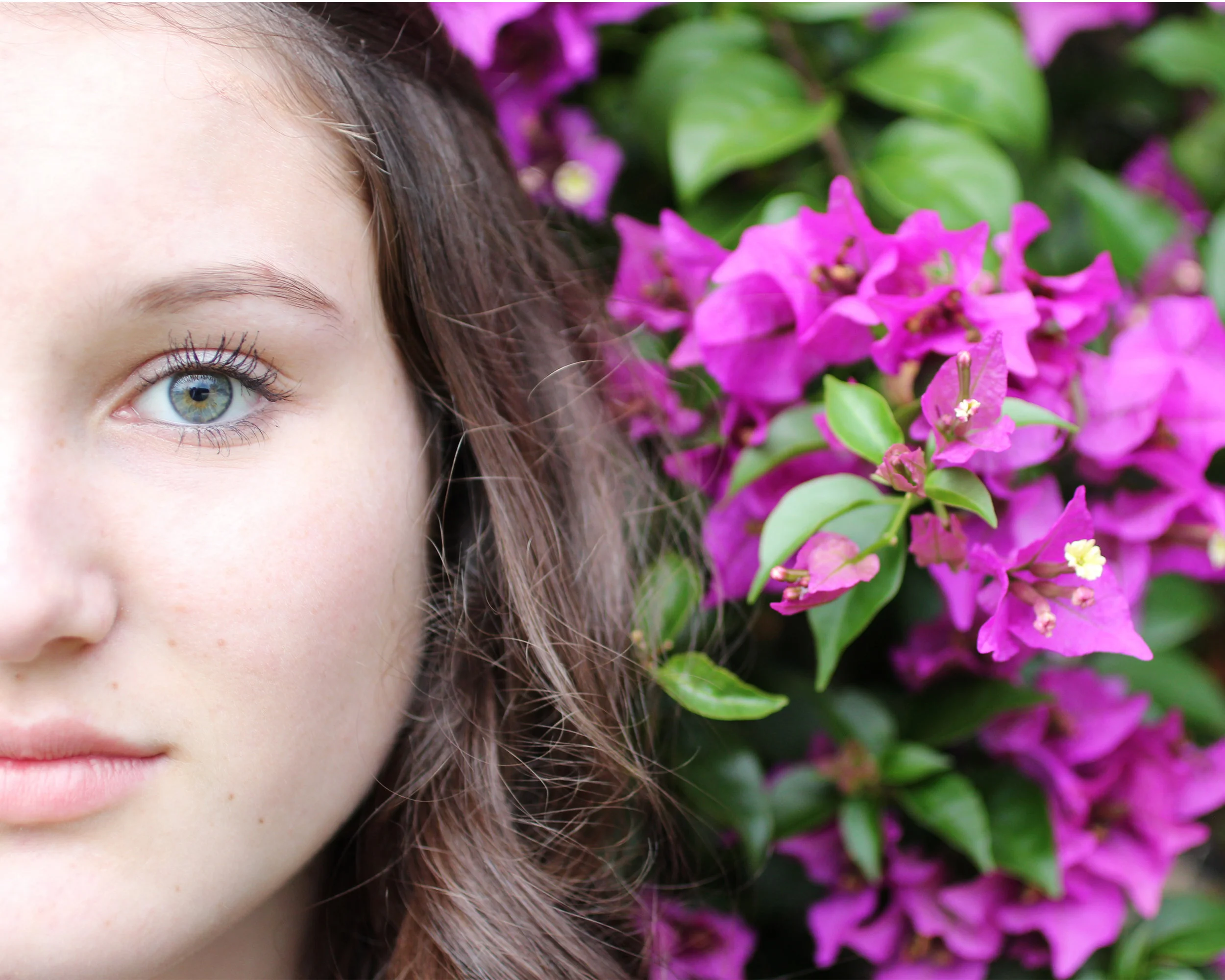 Self portrait of Summer Pesiri. Half of her face is in the frame. A bush with purple flowers is in the background.