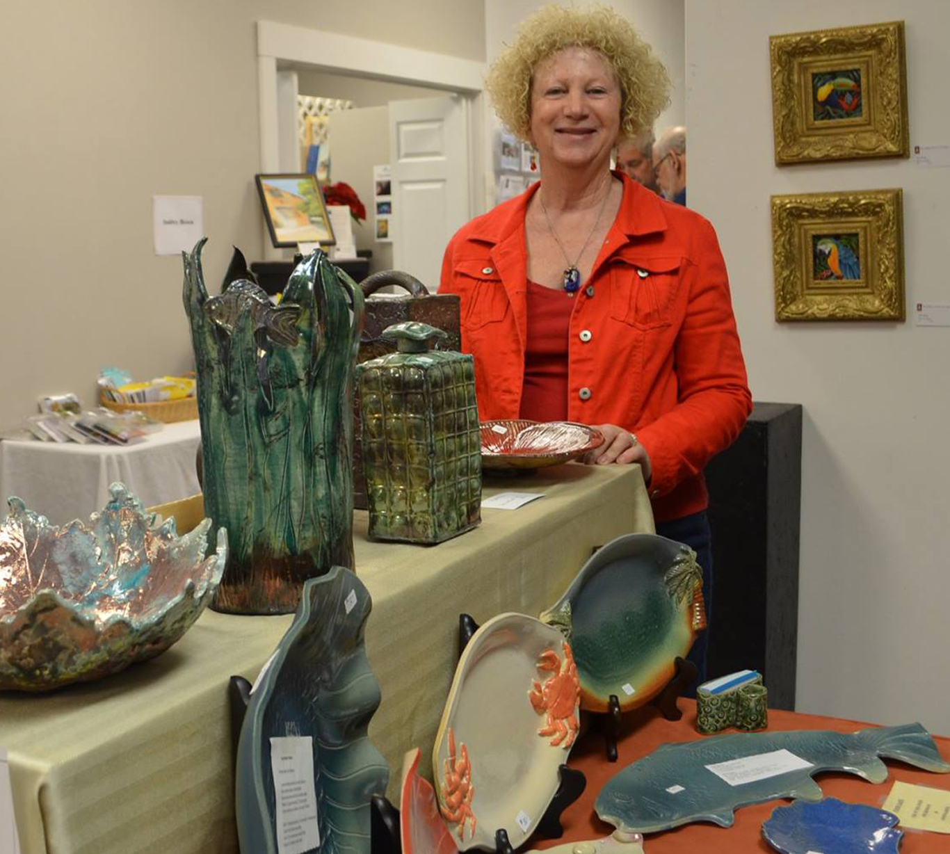 Portrait of a Robinn Wren standing next to various pottery pieces all on display in a gallery.
