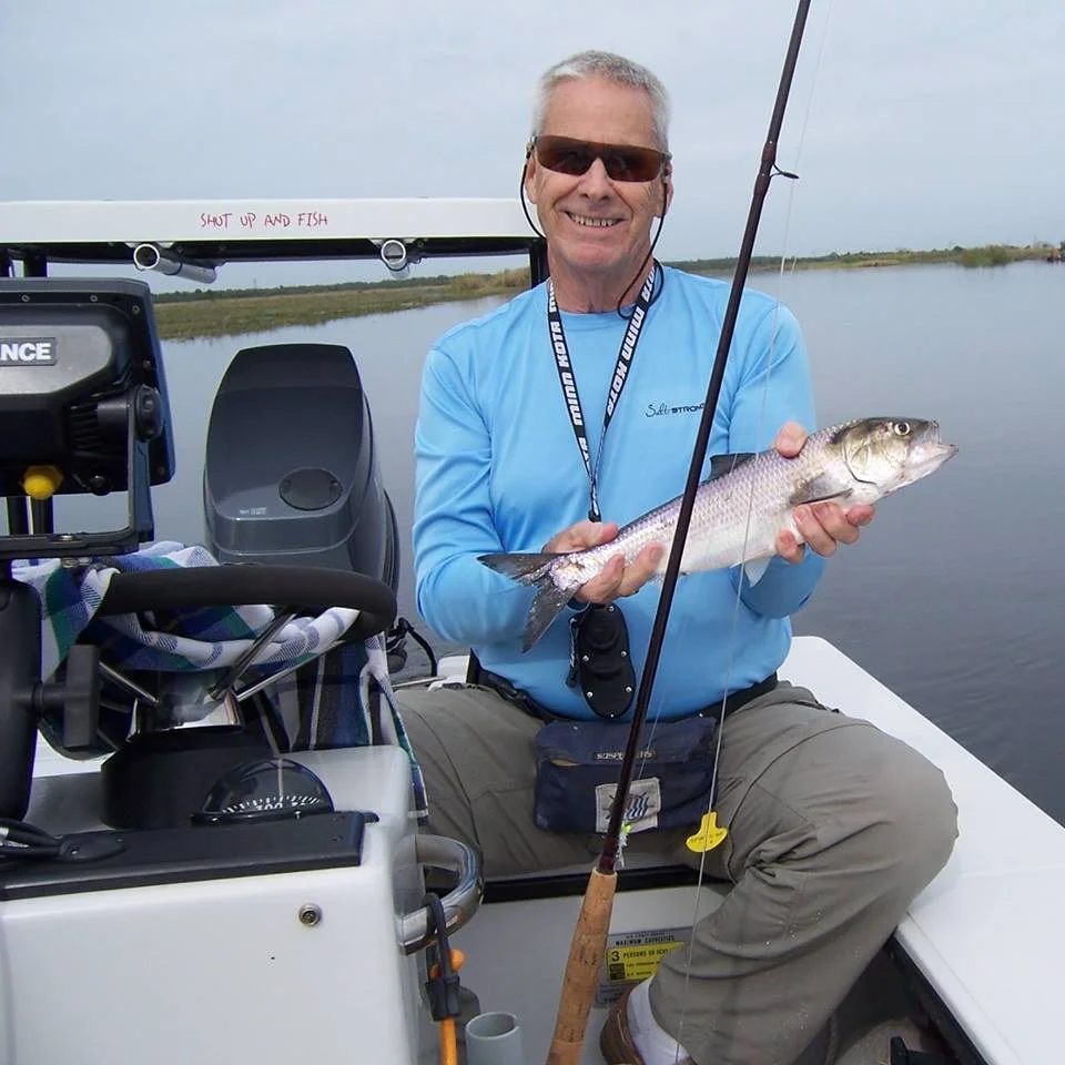 Portrait of Bil Meyers sitting on a boat holding a fish that he just caught.