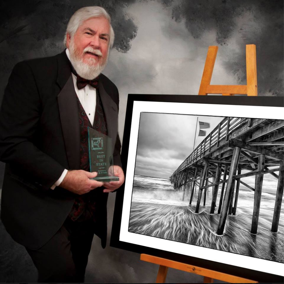 Photo of Joe Campanellie holding an award, standing in front of one of his photographs