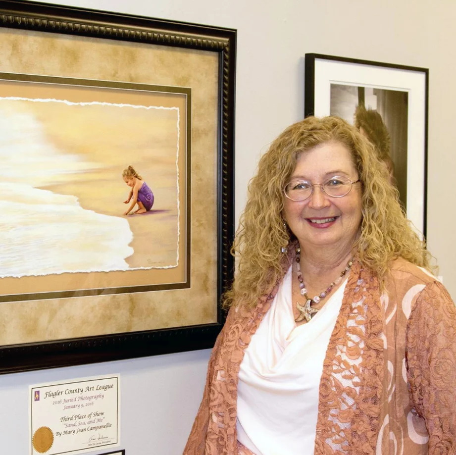 Portrait of Mary Jean Campanellie standing in front of one of her photographs.