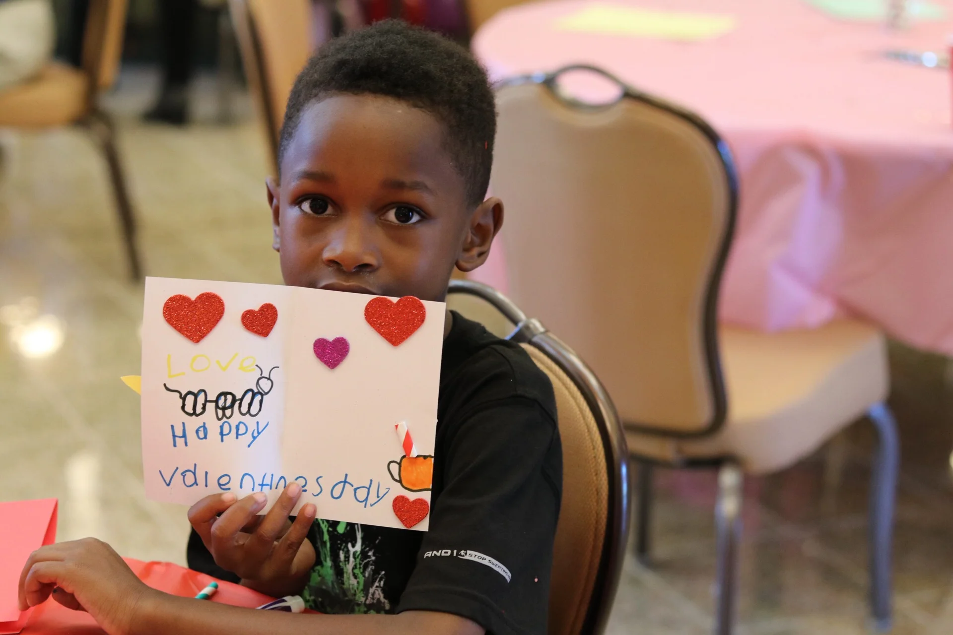 Young boy holding up a Happy Valentine's Day card.