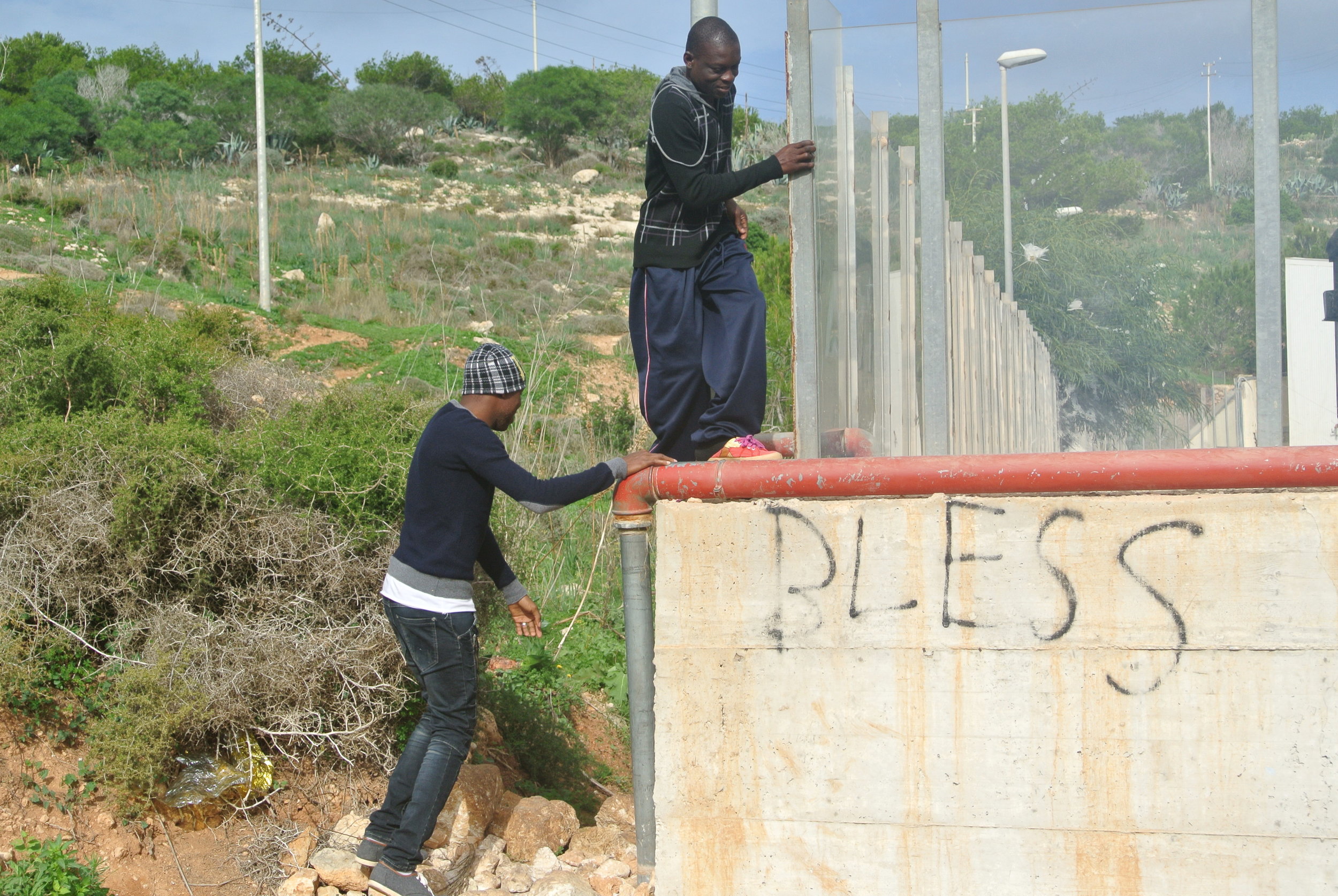  Migrants climb the outer wall to enter the hotspot. Lampedusa, Italy; November 2016. © Pamela Kerpius. 