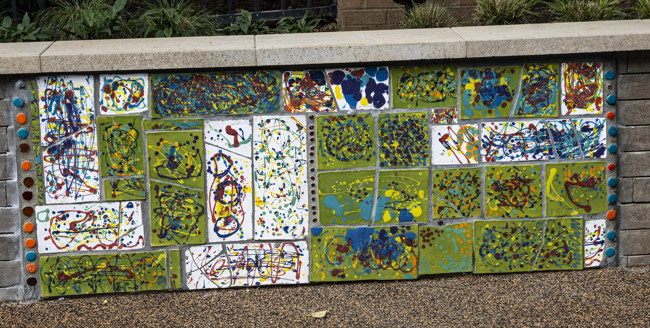  Abstract tile wall along the back left side of the playground, with glazed tiles&nbsp;created by students during an artist-led workshop in Jackson Pollock style. 