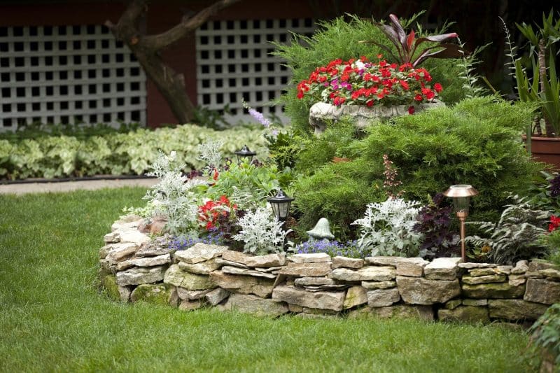 garden-path-resin-strip-edging-with-variety-of-perennial-foliage-in-flat-bed-and-raised-bed-with-dry-stacked-stone-edging-and-red-ti-plant-in-a-decorative-planter-and-brass-outdoor-lanterns-w.jpg