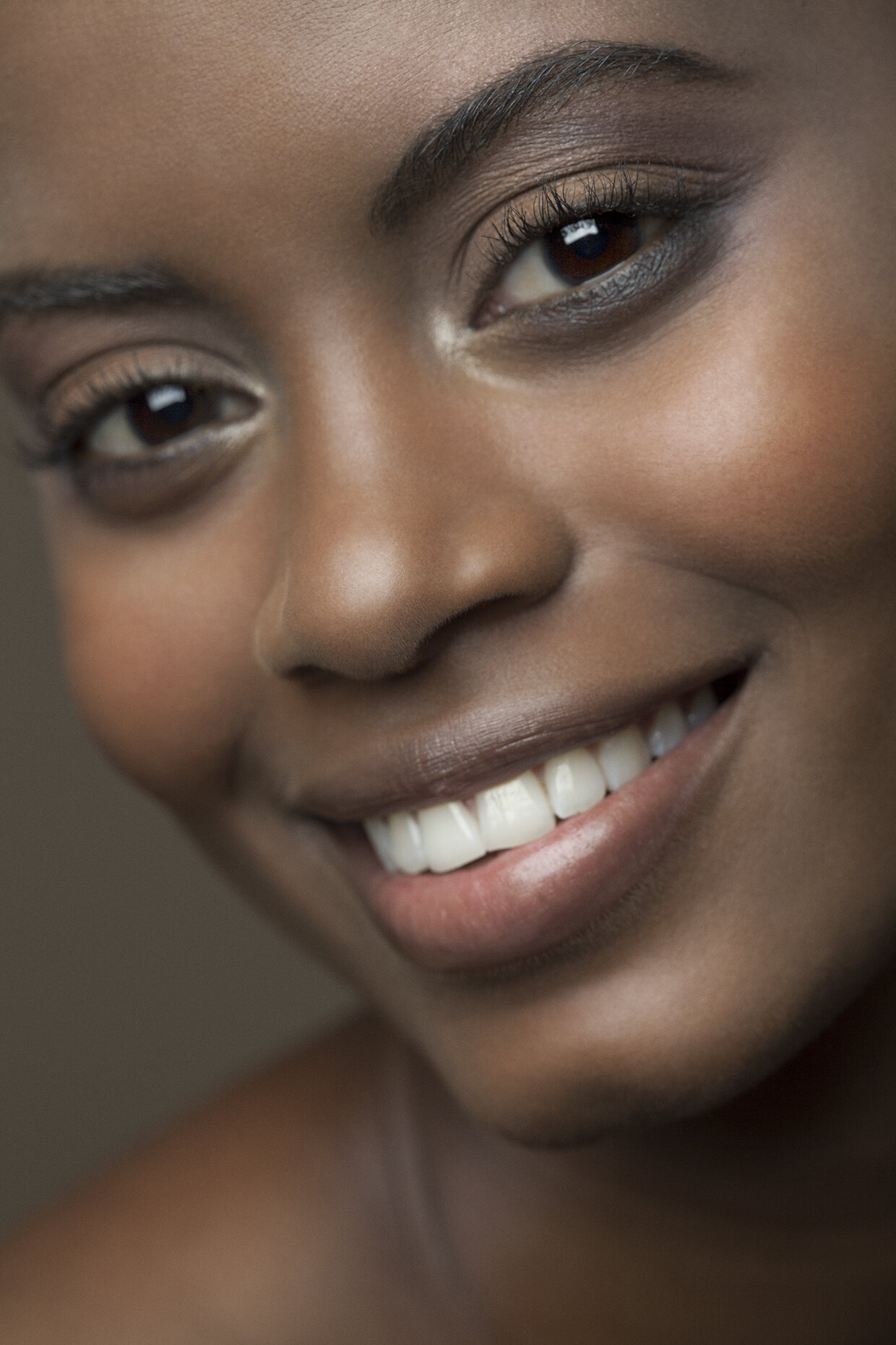 Close-up of smiling woman with dark skin, showing white teeth and bright eyes. Makeup by Leather & Lace Artistry in MA, RI, CT, NH, VT, and ME.