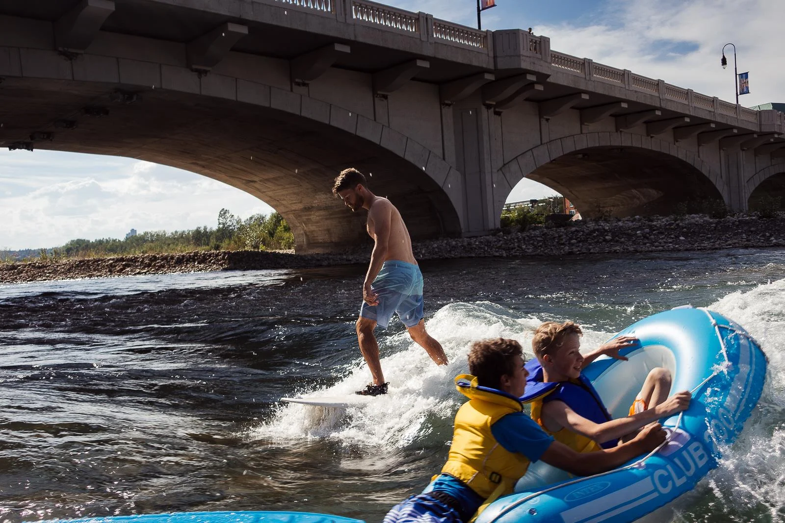 Rafting kids and a surfer at 10th Street Wave in Calgary