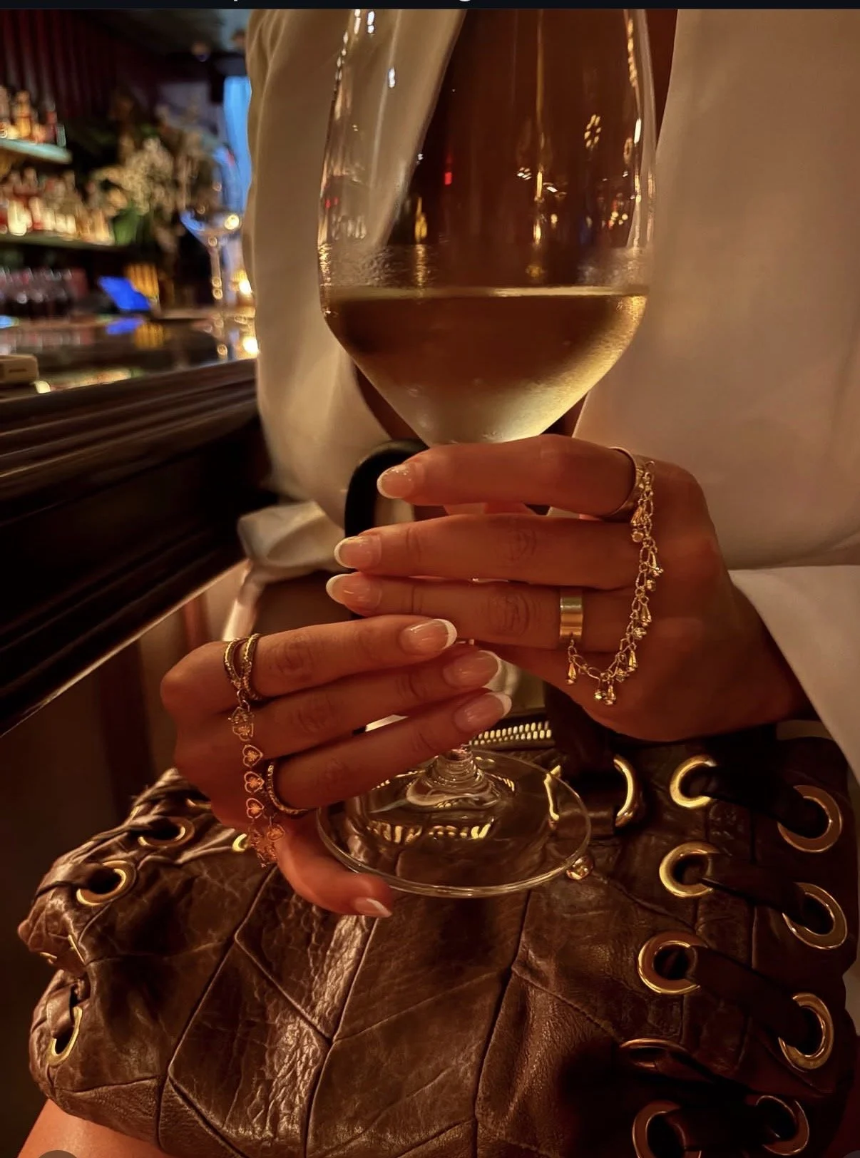 Woman holding a wine glass while wearing layered gold rings and hand jewelry by Amoura Jewelers.