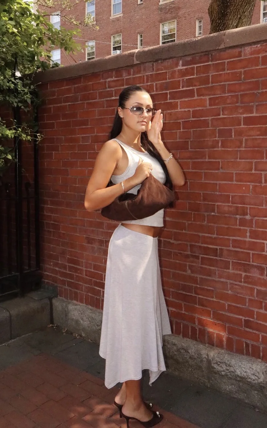 A woman holding the brown JAQ purse in front of a red brick wall.