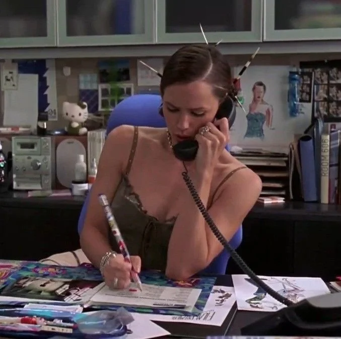 Jennifer Garner as Jenna Rink writing at a magazine desk while talking on the phone in 13 Going on 30.