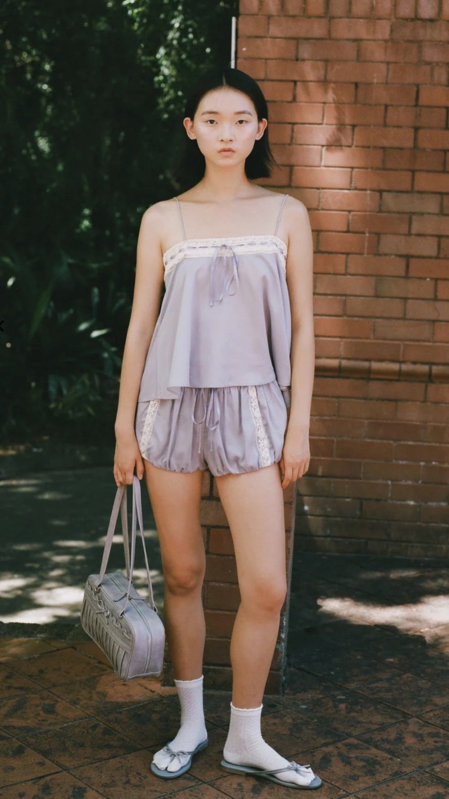1. Model wearing a lilac camisole and matching lace-trimmed bubble shorts, with white socks, pale blue bow flats, and a handbag outdoors.