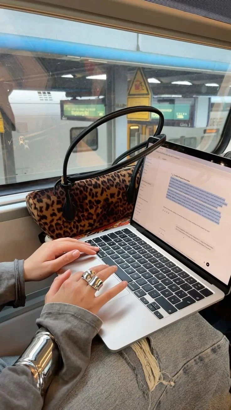 A woman working on a laptop beside a leopard-print handbag while travelling by train.