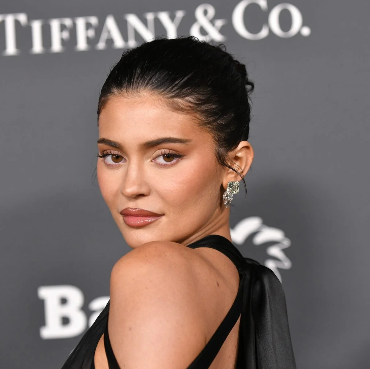 Kylie Jenner looks over her shoulder in a black outfit, with an updo and defined makeup, at the 2022 Baby2Baby Gala.